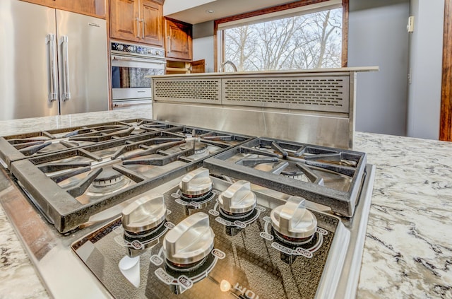 details featuring light stone counters, stainless steel appliances, and brown cabinets