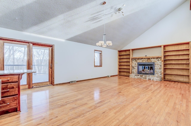 unfurnished living room featuring visible vents, light wood-style flooring, a stone fireplace, a textured ceiling, and a notable chandelier