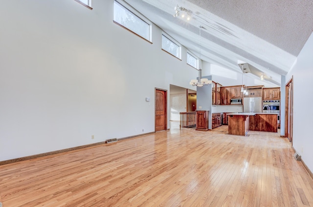 unfurnished living room with baseboards, visible vents, light wood-style floors, a textured ceiling, and a notable chandelier