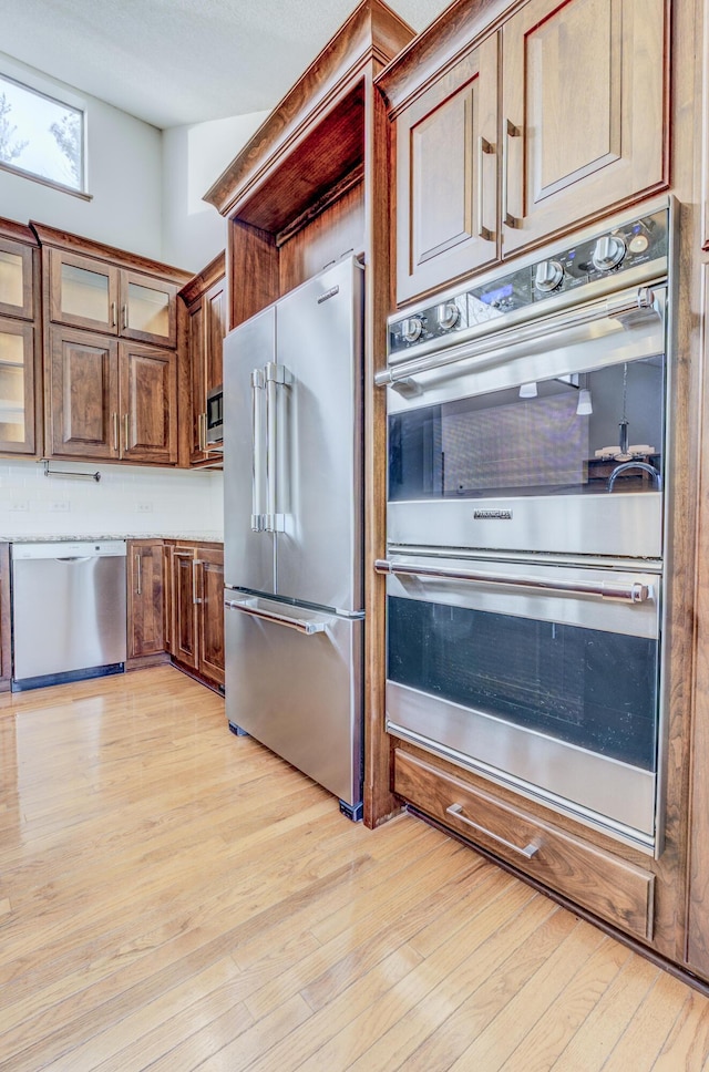 kitchen featuring glass insert cabinets, light wood-type flooring, and stainless steel appliances