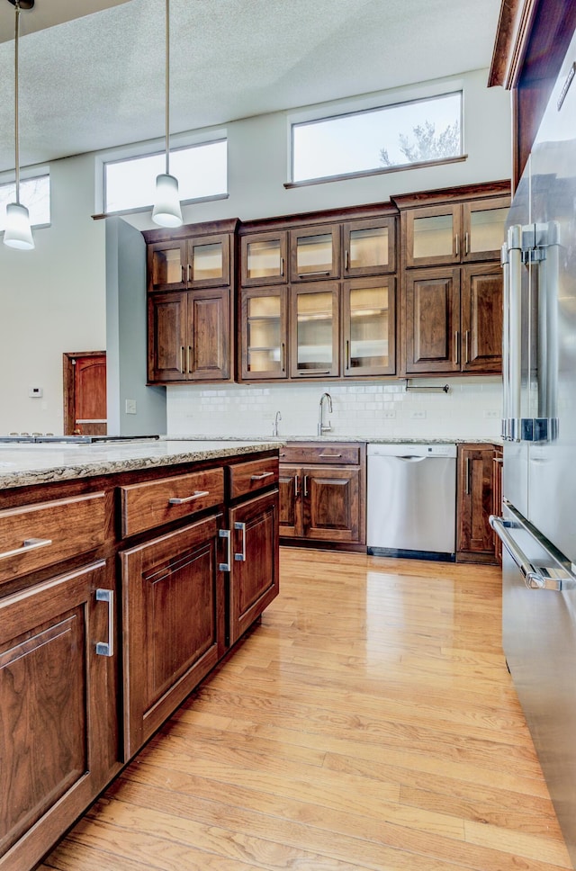 kitchen featuring light wood-type flooring, tasteful backsplash, appliances with stainless steel finishes, and hanging light fixtures