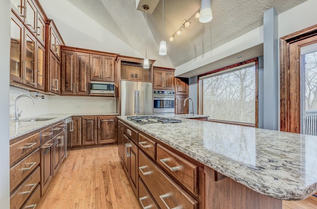 kitchen featuring lofted ceiling, light stone counters, appliances with stainless steel finishes, light wood-style floors, and a sink