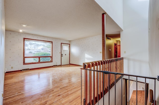 foyer entrance featuring visible vents, wallpapered walls, baseboards, and wood finished floors