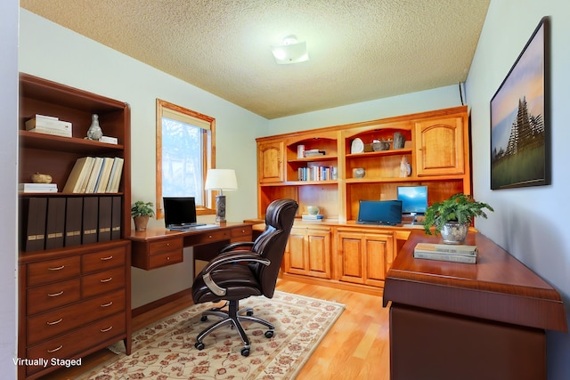 home office with a textured ceiling, light wood-style floors, and built in study area