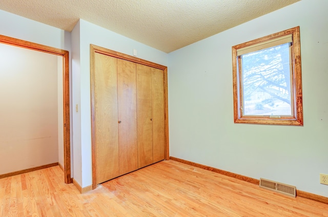 unfurnished bedroom with light wood-style floors, visible vents, a closet, and a textured ceiling