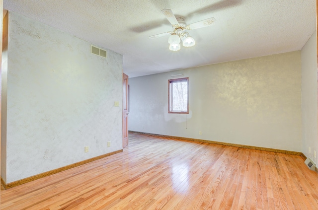 spare room featuring visible vents, a textured ceiling, wood finished floors, baseboards, and ceiling fan