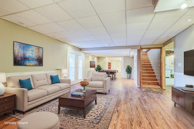 living area with a paneled ceiling, stairs, and light wood-style floors