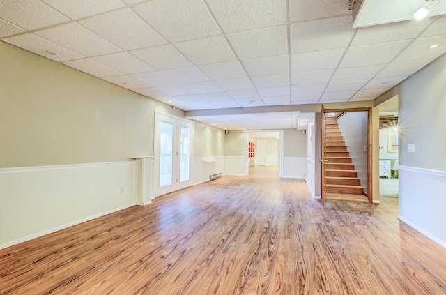 unfurnished living room featuring stairway, light wood-style floors, baseboards, and a drop ceiling