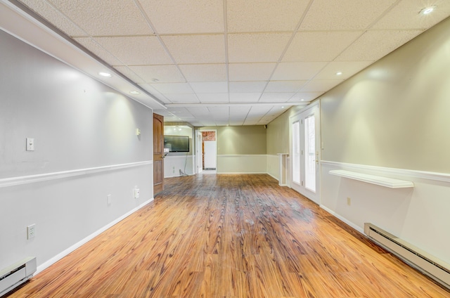 empty room with a drop ceiling, wood finished floors, baseboards, and baseboard heating