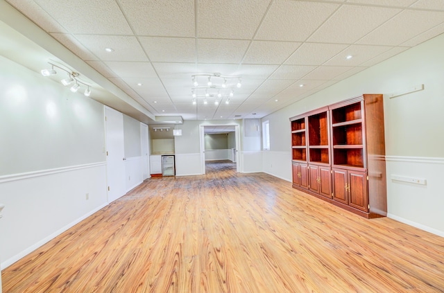 unfurnished living room with baseboards, a paneled ceiling, track lighting, and light wood finished floors