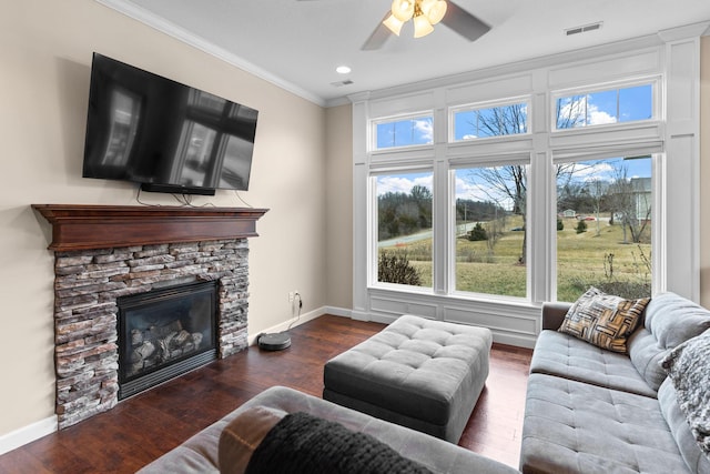 living room with crown molding, a stone fireplace, dark hardwood / wood-style floors, and ceiling fan