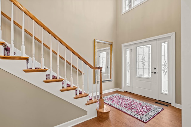 foyer with a towering ceiling, wood finished floors, visible vents, and baseboards