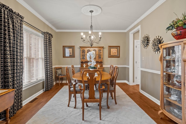 dining space with an inviting chandelier, visible vents, wood finished floors, and ornamental molding