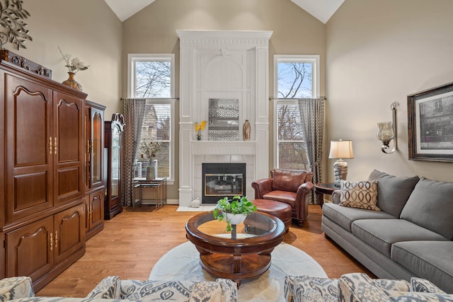 living room featuring light wood-type flooring, a healthy amount of sunlight, high vaulted ceiling, and a tile fireplace