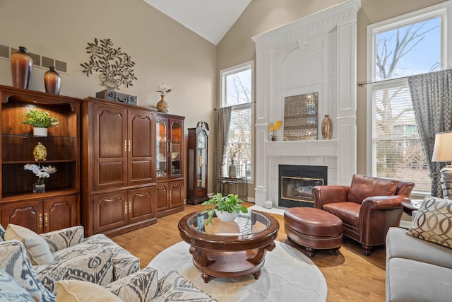 living area with high vaulted ceiling, visible vents, light wood finished floors, and a tiled fireplace