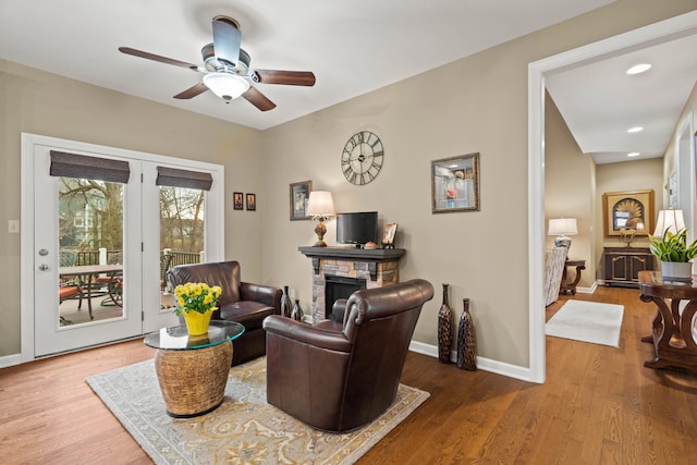 sitting room featuring a ceiling fan, baseboards, wood finished floors, and a stone fireplace