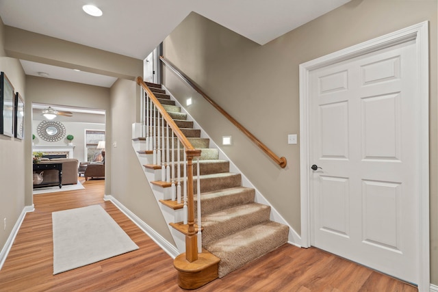 stairway with ceiling fan, a fireplace, wood finished floors, and baseboards