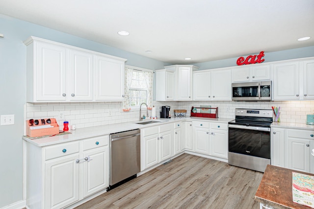 kitchen with stainless steel appliances, a sink, light wood-type flooring, backsplash, and white cabinets