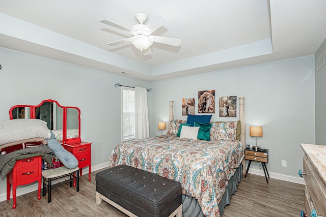 bedroom with wood finished floors, baseboards, and a tray ceiling