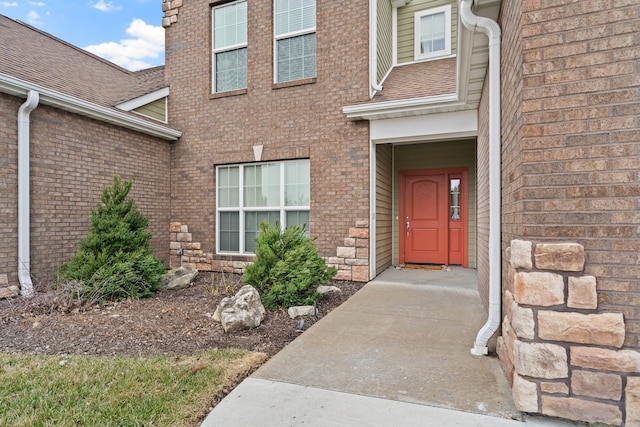 doorway to property with brick siding and roof with shingles