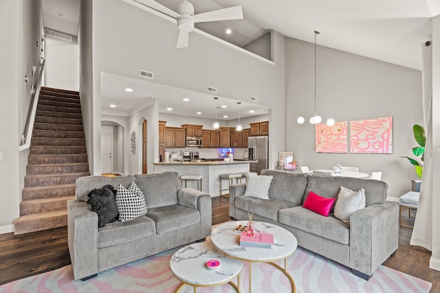 living area featuring dark wood-type flooring, ceiling fan with notable chandelier, visible vents, and stairs