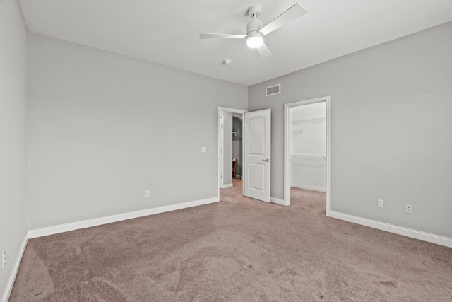 unfurnished bedroom featuring carpet, a walk in closet, a closet, visible vents, and baseboards