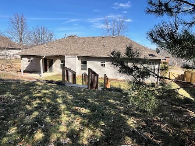 back of house with roof with shingles, fence, a patio, and a lawn