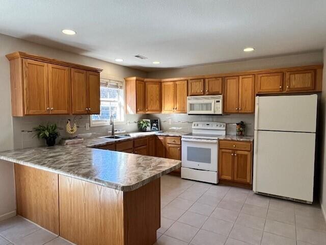 kitchen featuring a peninsula, white appliances, a sink, and brown cabinets