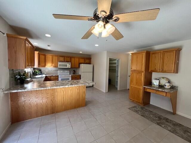 kitchen featuring a peninsula, white appliances, brown cabinetry, and built in desk