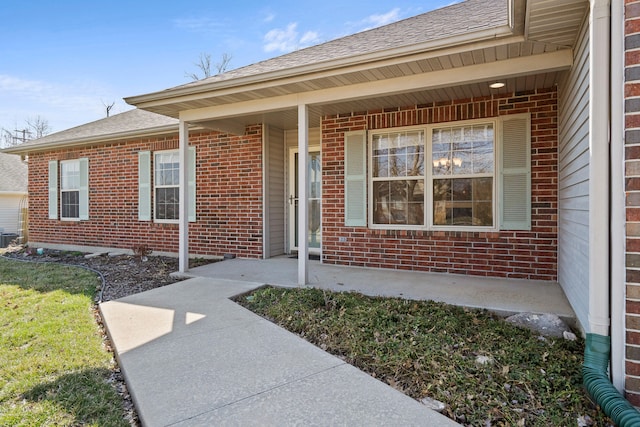 property entrance with brick siding, a porch, and roof with shingles