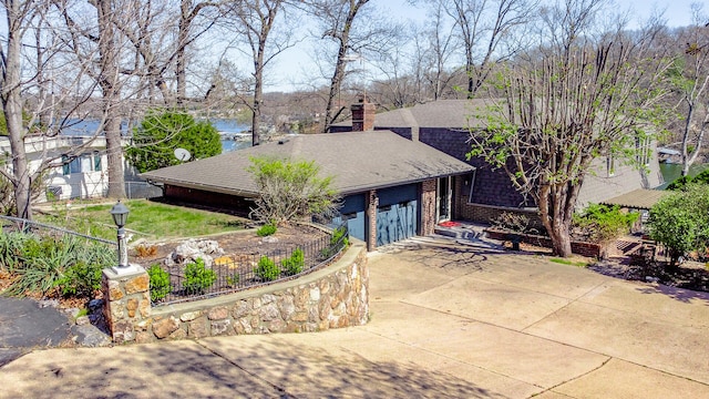 view of front facade with a shingled roof, a water view, fence, driveway, and a chimney