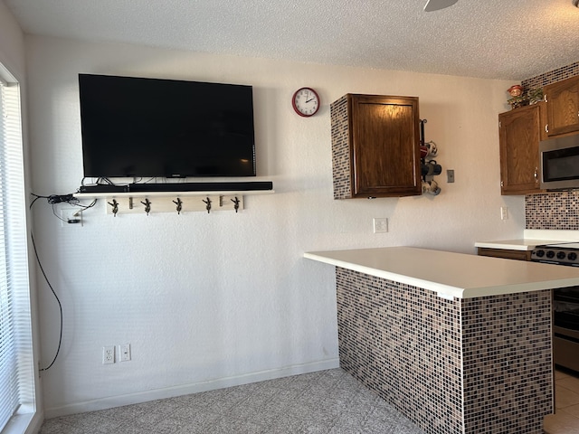 interior space featuring range, dark brown cabinets, a textured ceiling, decorative backsplash, and kitchen peninsula