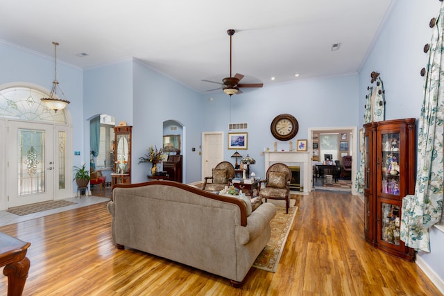 living room with a high ceiling, ornamental molding, ceiling fan, and light wood-type flooring