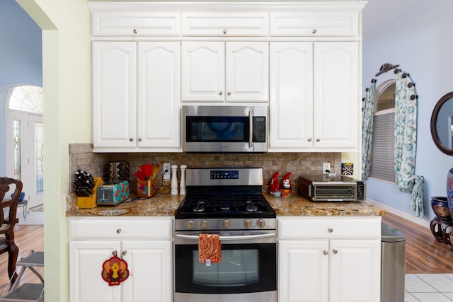 kitchen featuring stainless steel appliances, tasteful backsplash, white cabinets, and dark stone counters