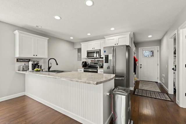 kitchen featuring dark wood-style floors, light countertops, appliances with stainless steel finishes, white cabinetry, and a peninsula