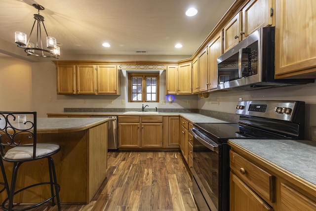 kitchen with stainless steel appliances, dark hardwood / wood-style flooring, decorative light fixtures, sink, and a kitchen breakfast bar