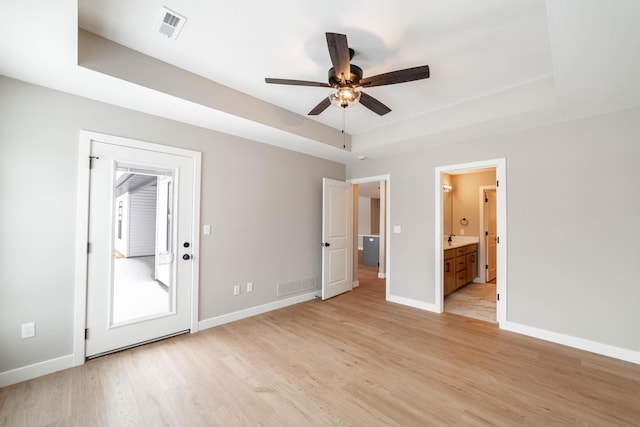 unfurnished bedroom with ensuite bathroom, light hardwood / wood-style floors, a tray ceiling, and ceiling fan