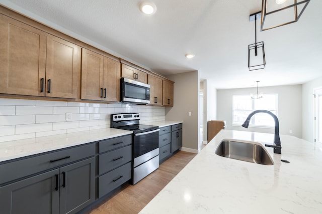 kitchen with appliances with stainless steel finishes, tasteful backsplash, light stone counters, decorative light fixtures, and sink