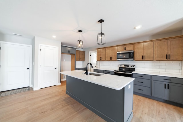 kitchen with appliances with stainless steel finishes, hanging light fixtures, an island with sink, light stone countertops, and sink