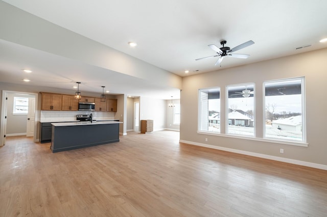 kitchen with a center island with sink, stainless steel appliances, hanging light fixtures, light hardwood / wood-style flooring, and decorative backsplash