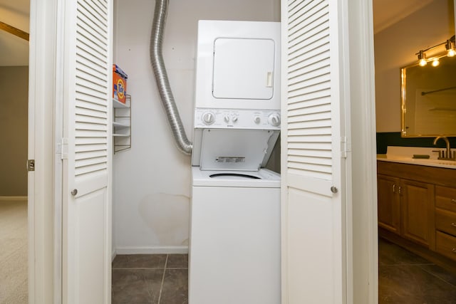 clothes washing area featuring dark tile patterned flooring, stacked washer and clothes dryer, and sink