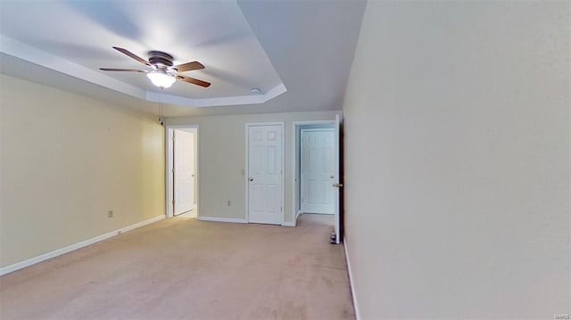 carpeted spare room with a tray ceiling and ceiling fan