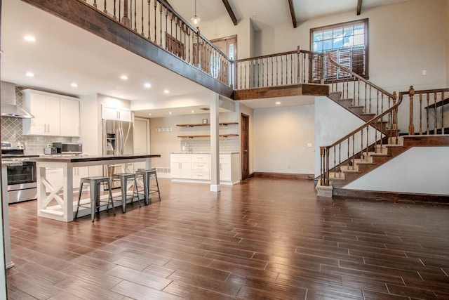 living area with dark wood-style floors, beamed ceiling, baseboards, and stairs