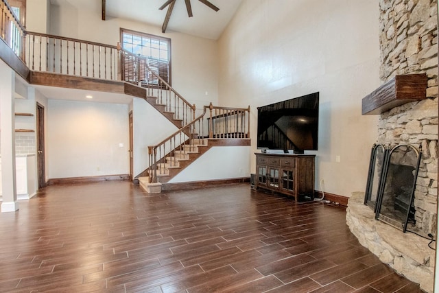 unfurnished living room with wood finish floors, a fireplace, a towering ceiling, baseboards, and stairway