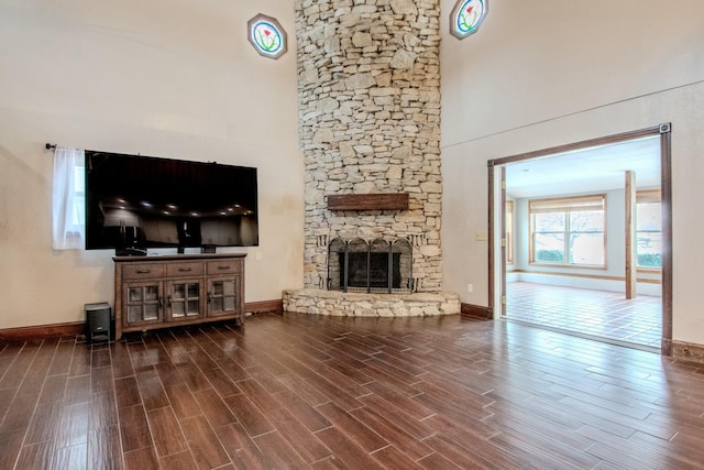 living room with wood tiled floor, a fireplace, a towering ceiling, and baseboards