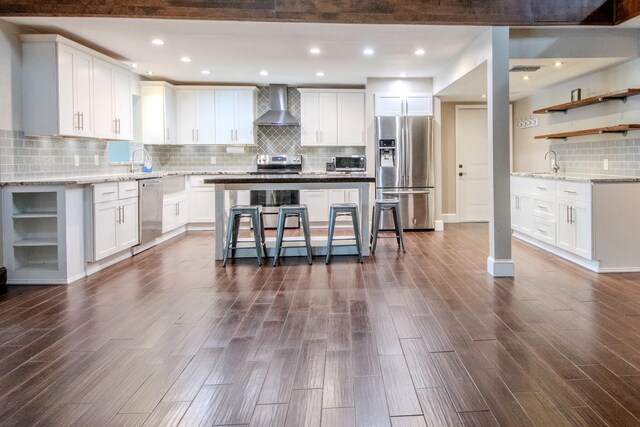 kitchen with a sink, stainless steel appliances, wall chimney range hood, and open shelves