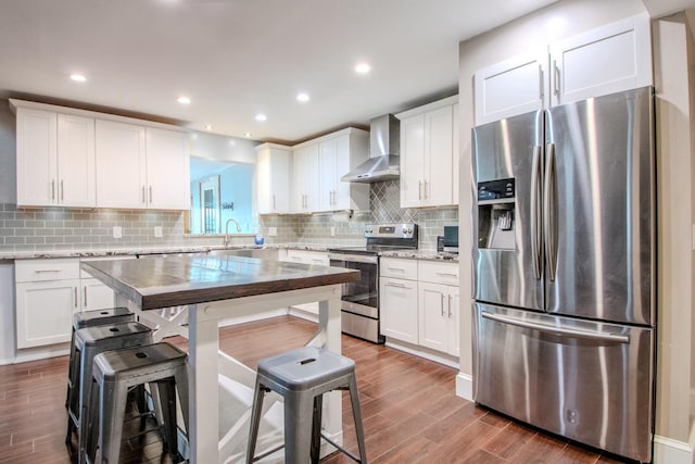 kitchen with stainless steel appliances, backsplash, dark wood-type flooring, white cabinets, and wall chimney range hood