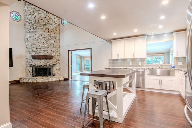 kitchen with dark wood-style flooring, a fireplace, stainless steel dishwasher, open floor plan, and white cabinetry