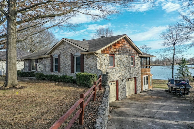 view of side of property with a garage, stone siding, concrete driveway, and a water view