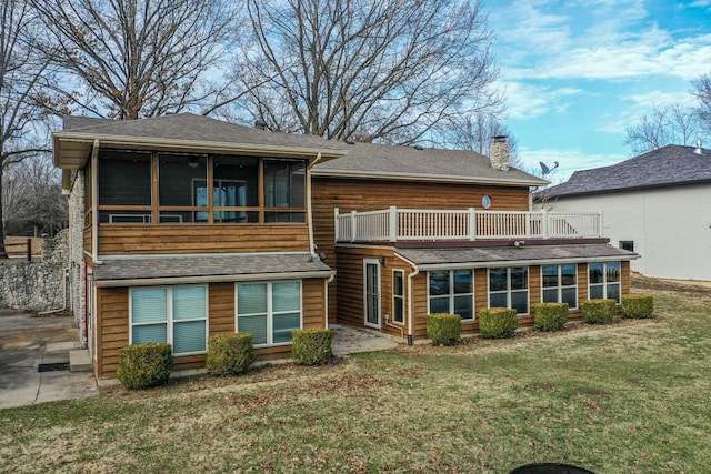 rear view of house with roof with shingles, a lawn, a chimney, and a sunroom